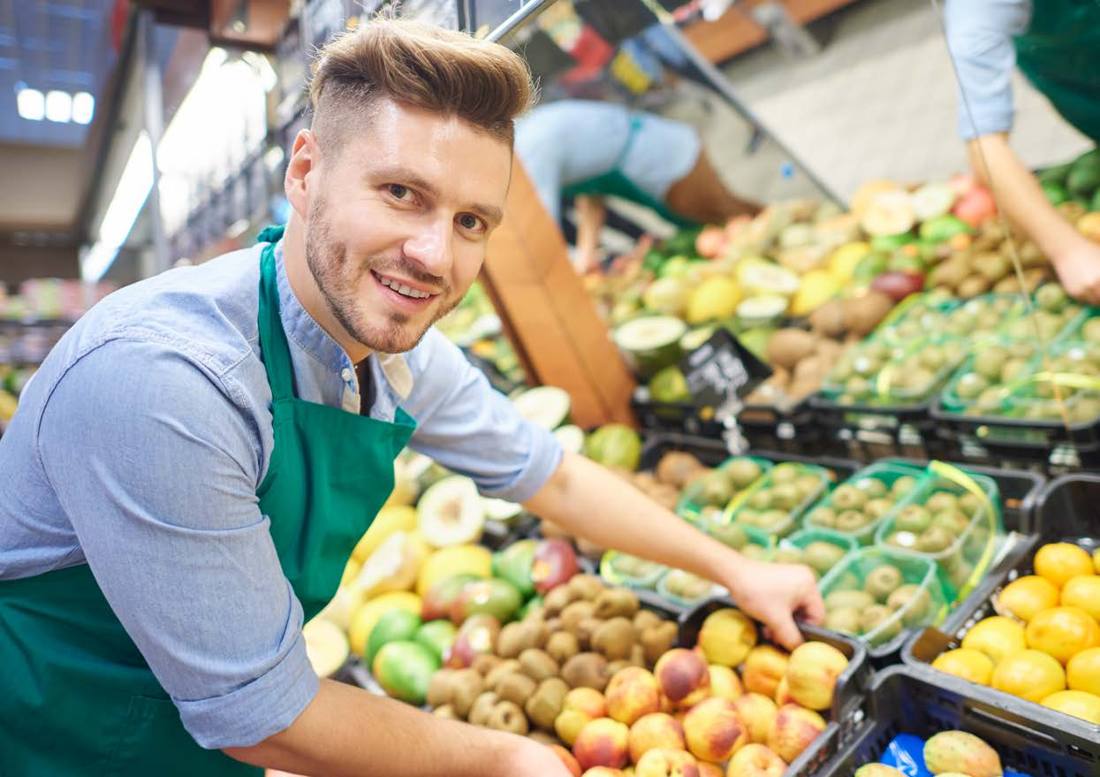 A smiling shop assistant arranging fruit